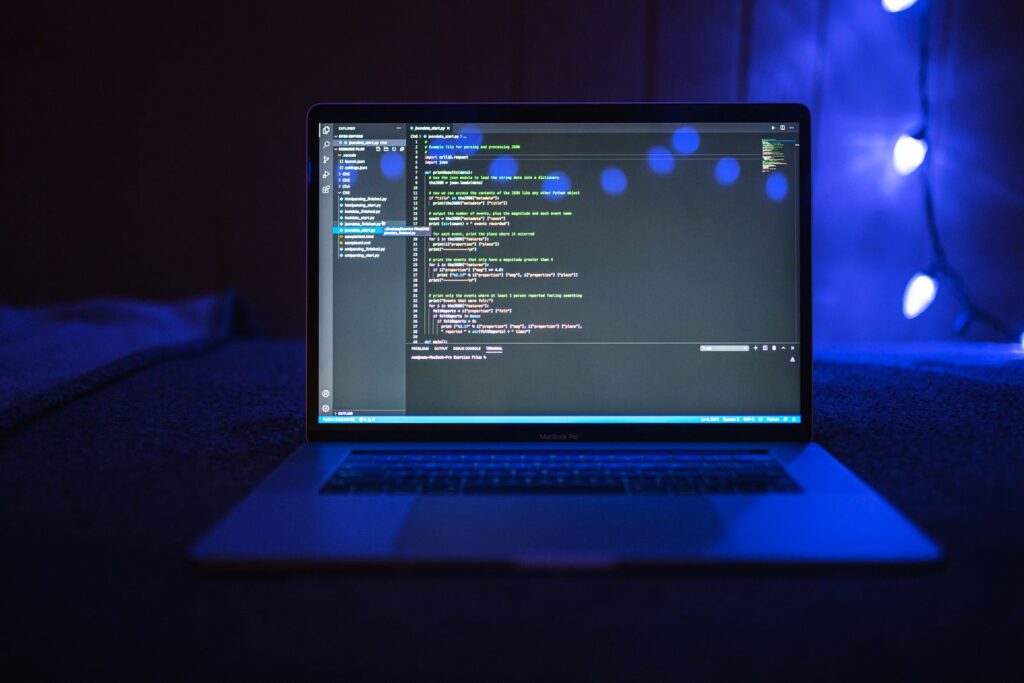 Laptop showing lines of program code in a dark room with blue lighting